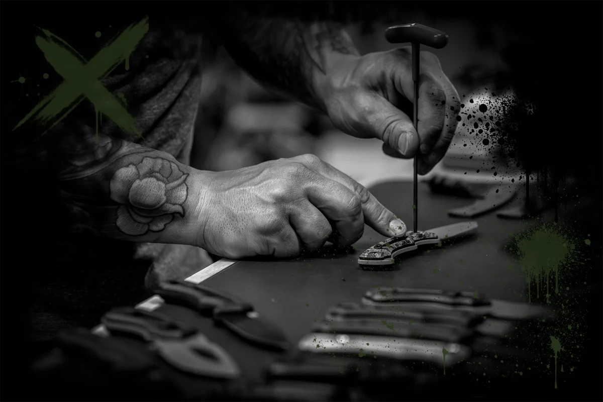 Hands assembling a HAViK knife on the workbench, with finished knives laid out in front